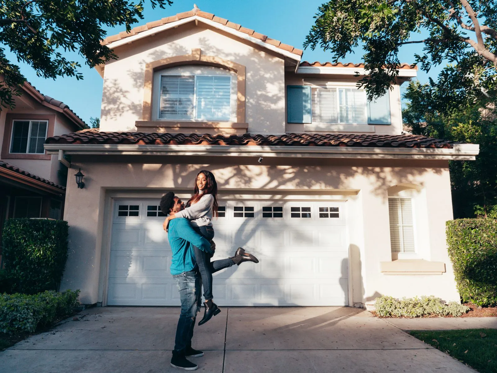 Joyful couple embracing in front of their new suburban house on a sunny day.